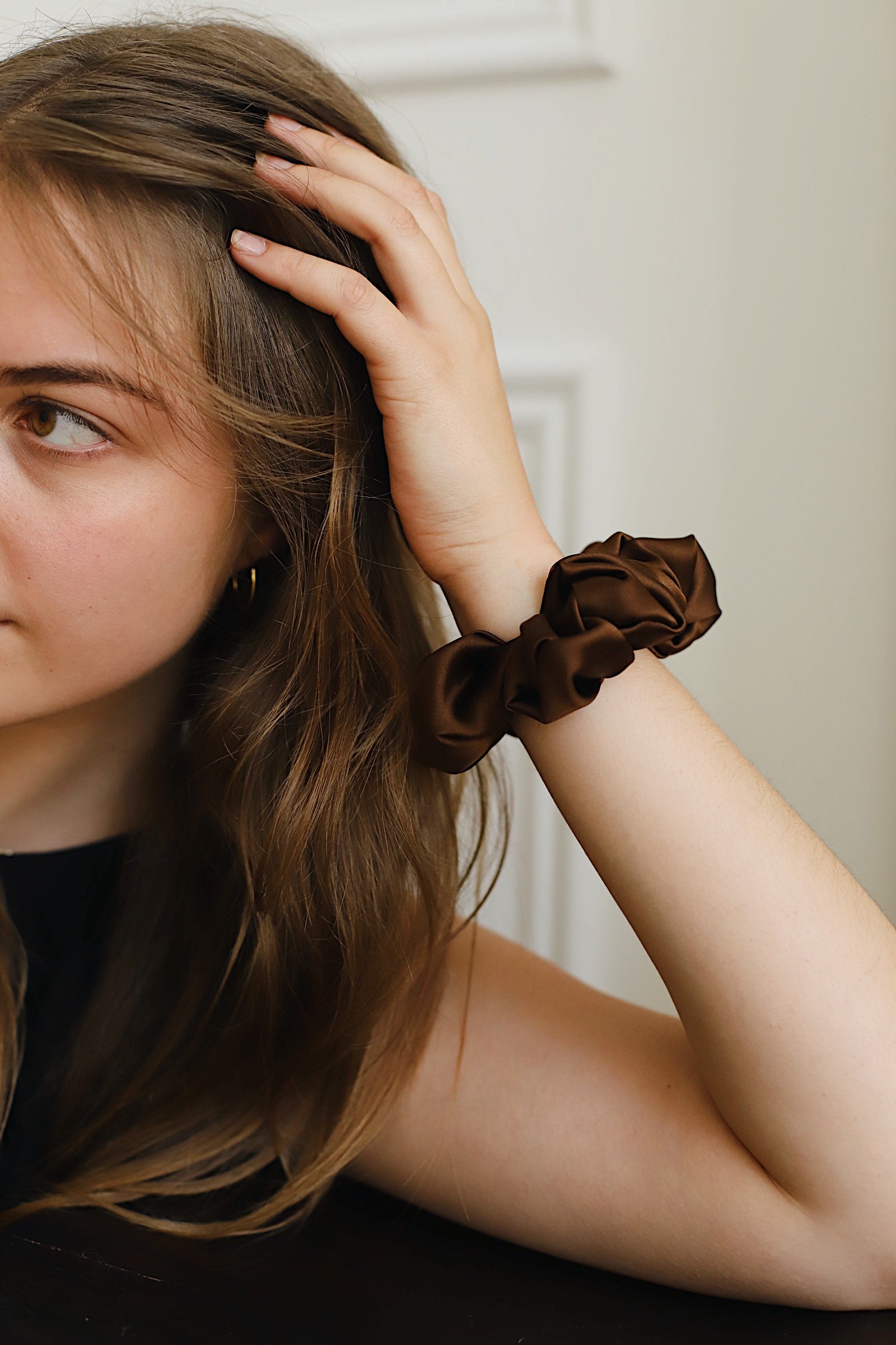 Close up of brown silk scrunchie on model's wrist. Model's hand is gently running through her hair