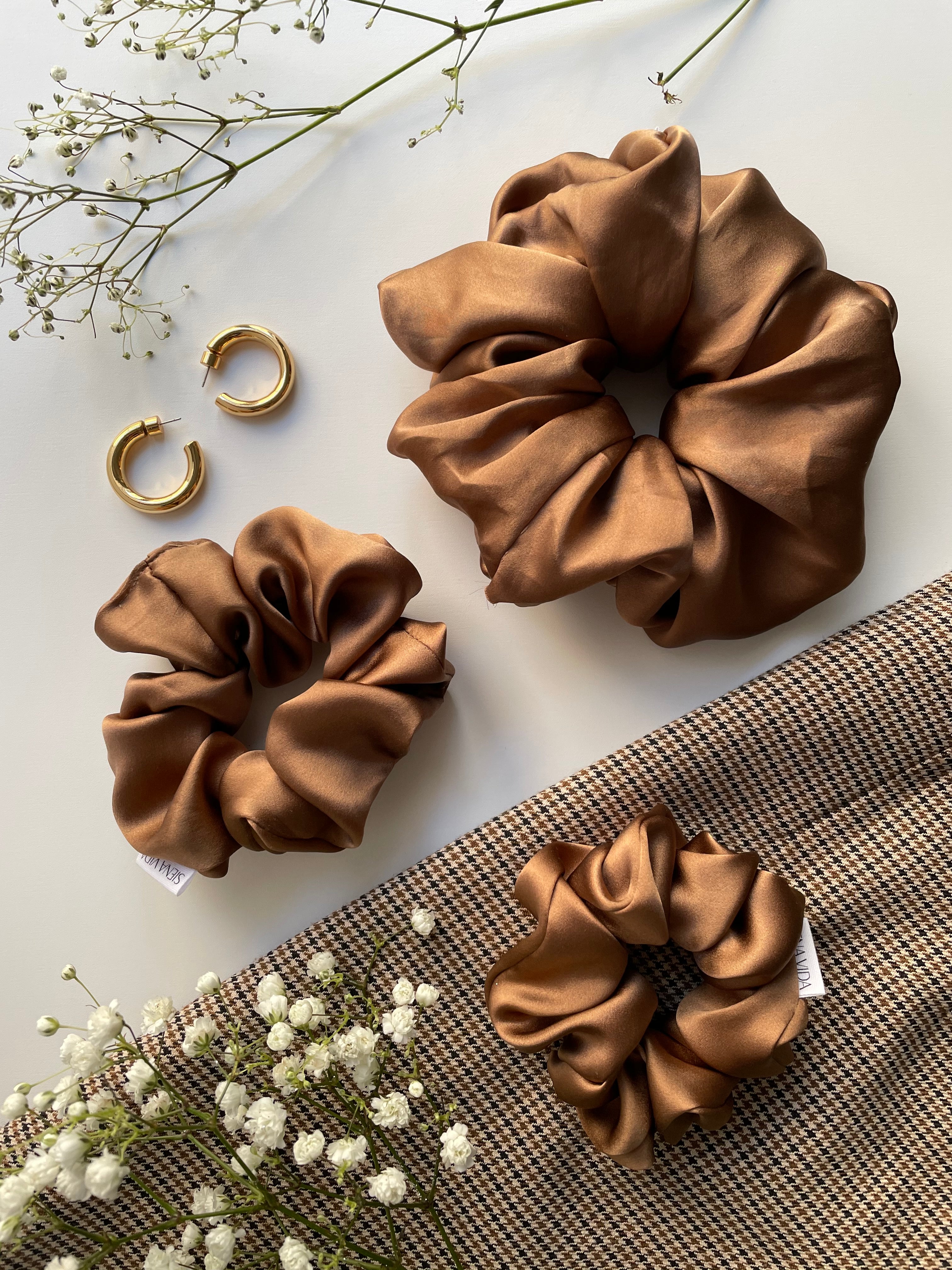 Nutmeg light brown silk scrunchie in Classic size and Cloud size beside gold hoop earrings and baby's breath floral.