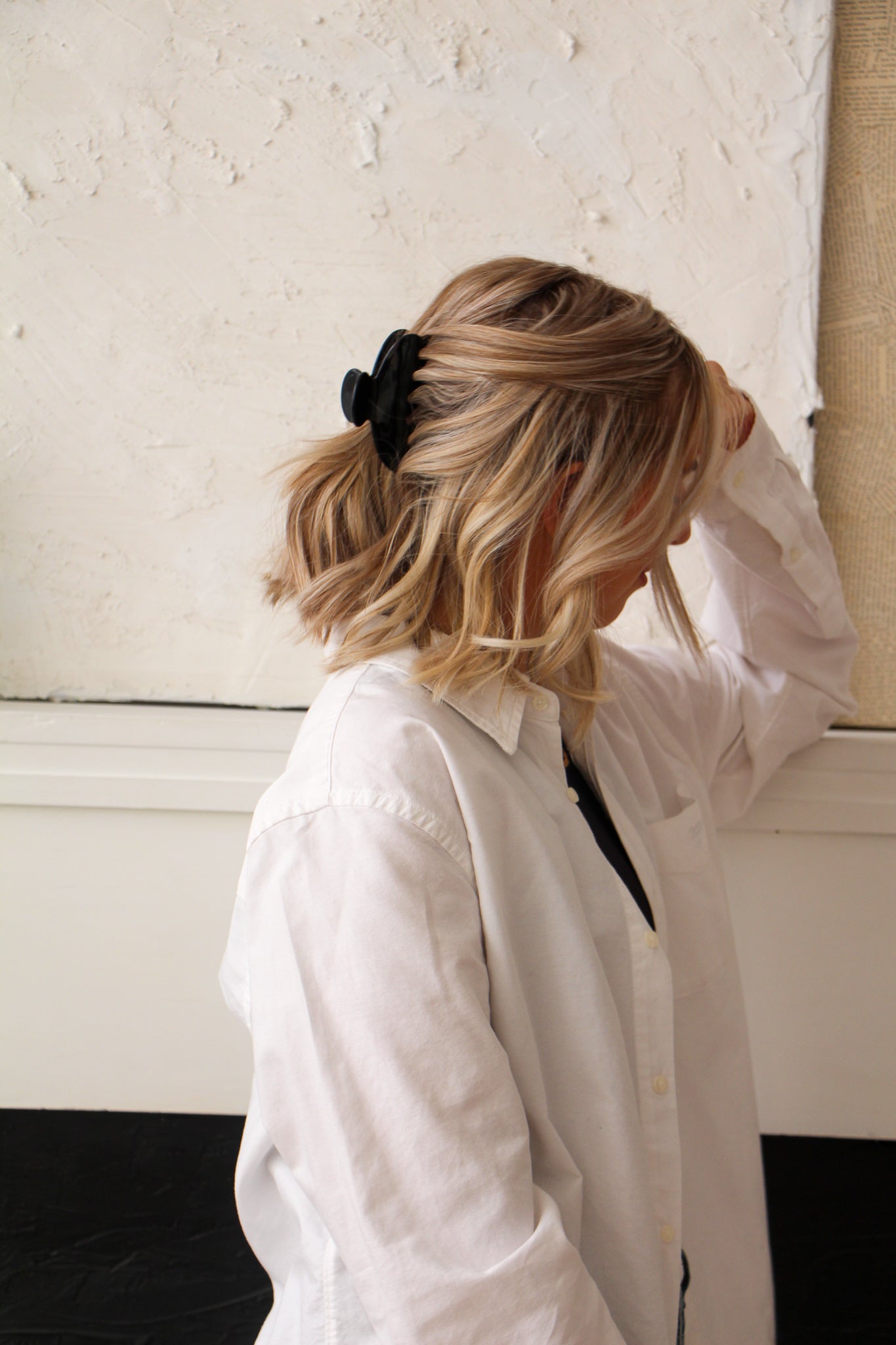 Black Claw Clip in model's half up hair style. Model is wearing a white dress shirt and leaning against a white fireplace. 