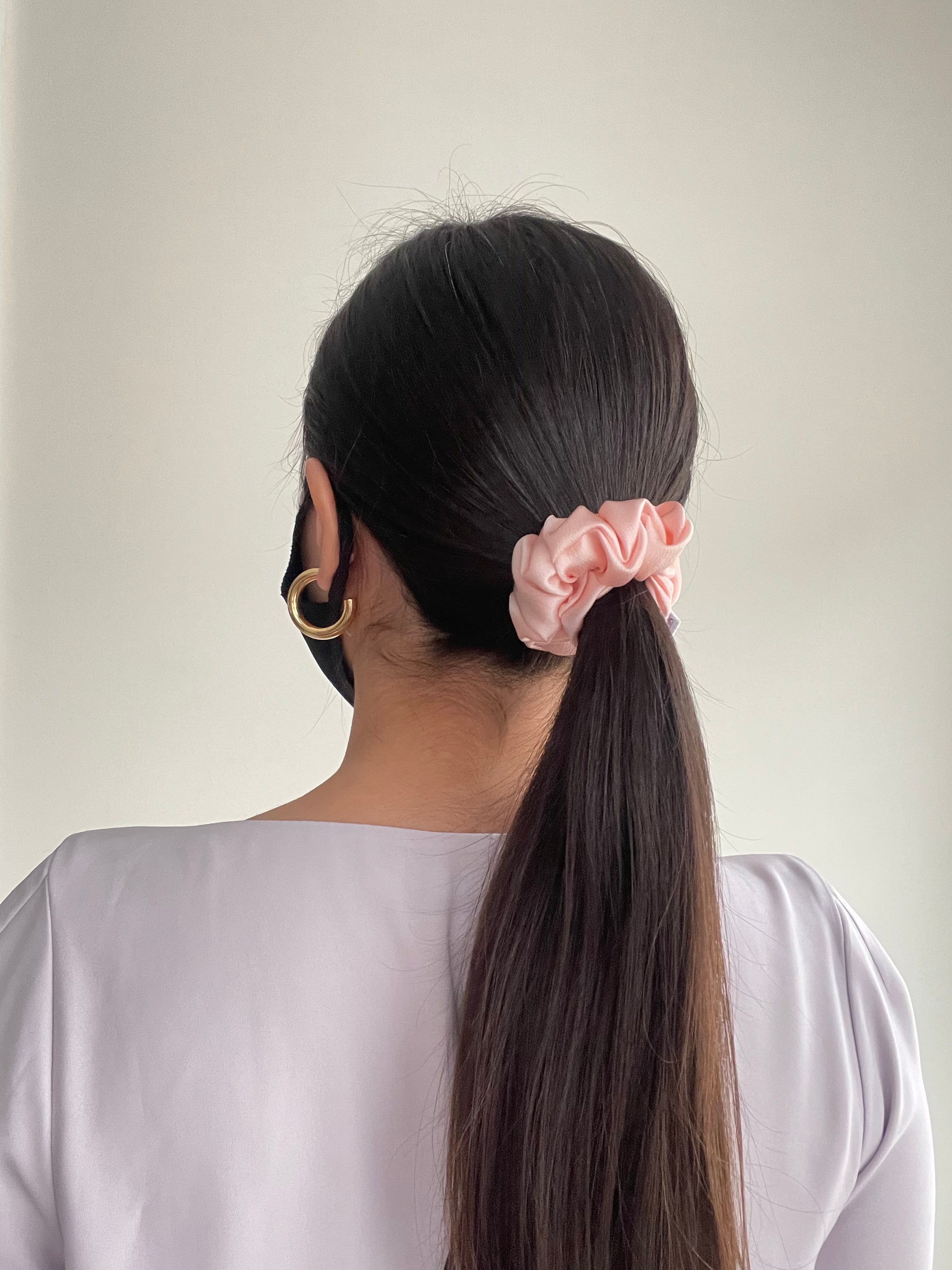 Thin pink silk scrunchie in model's ponytail